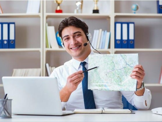 Travel agent wearing a headset and holding a map while pointing at it, suggesting travel guidance or consultancy.