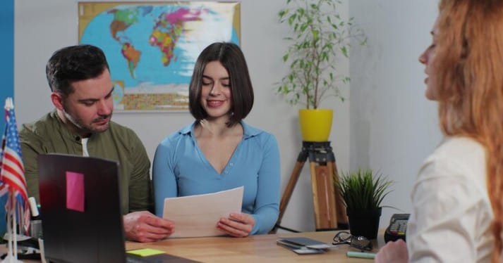 A couple consulting with a female travel agent in an office. The man is holding a document, and the woman is smiling, indicating a discussion or planning of a trip. 